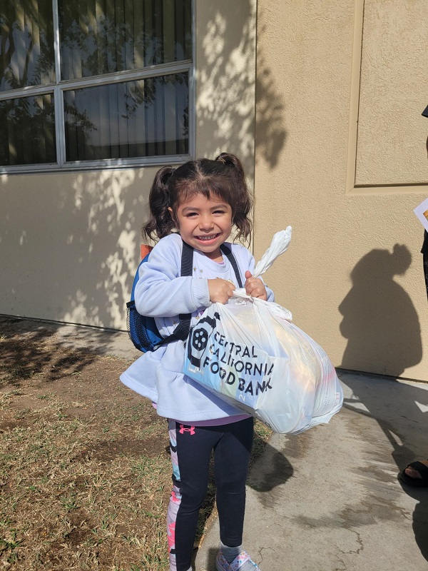 Little girl smiling and holding a bag from the Central California Food Bank